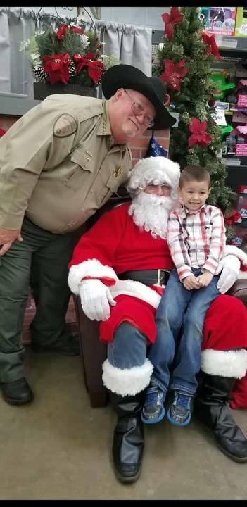 Sheriff with Santa who has a child on his lap