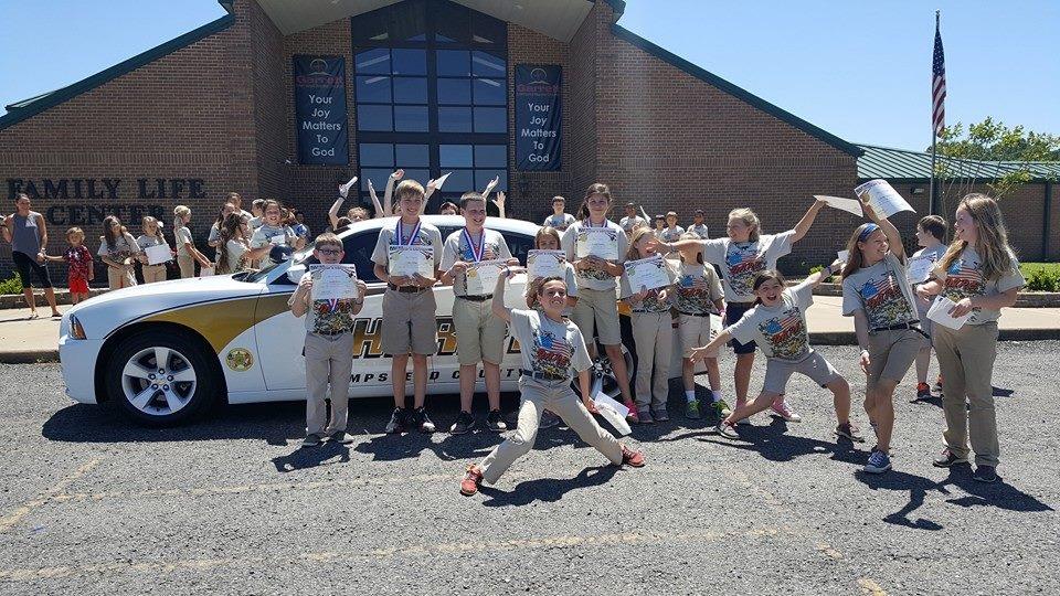 Students standing with sheriff vehicle in front of school