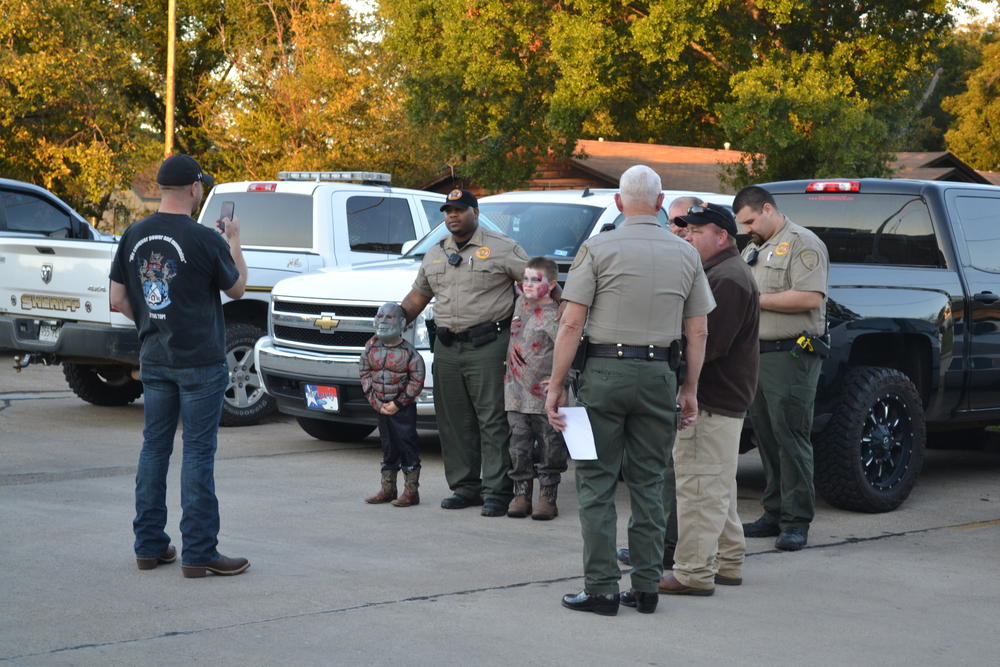 Officer standing witha  few kids trunk or treating