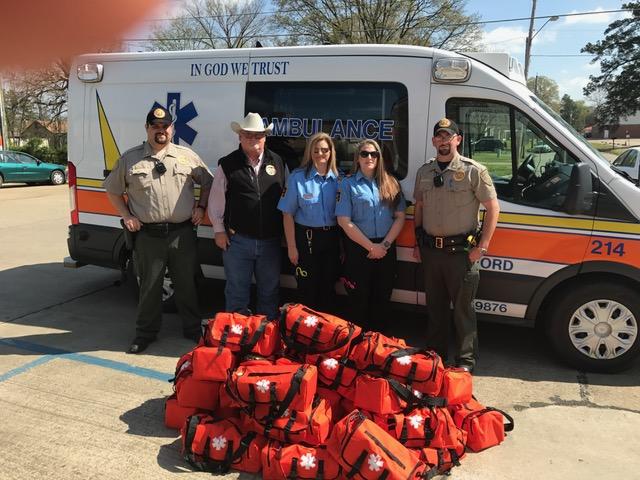 Paramedics and Sheriff's Office staff standing behind 25 trauma bags and in front of an ambulance