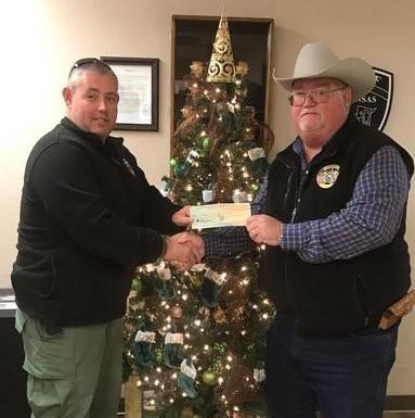 Sheriff Singleton and Dennis Hovarter shaking hands and holding check in front of christmas tree