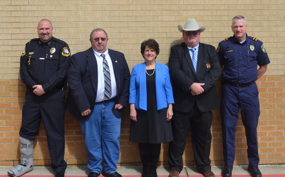 Four men and a woman standing in suits in front of brick wall