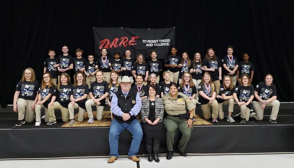 Large group of students with Sheriff's Office staff in front of DARE sign