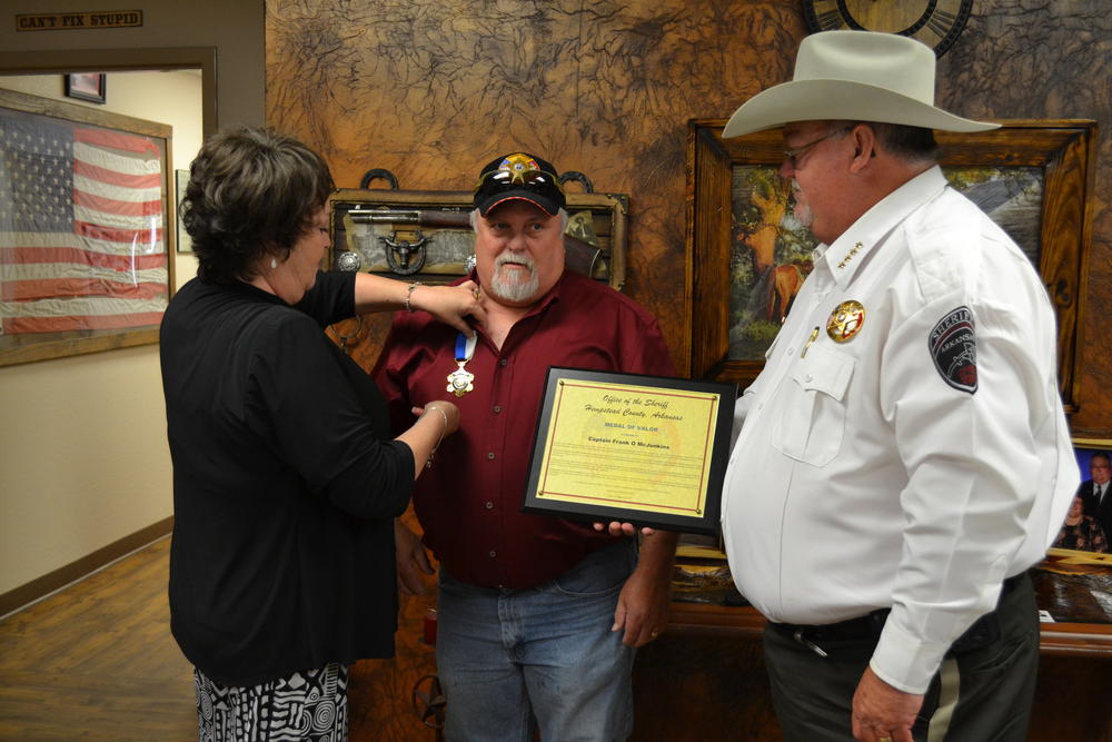 Kim McJunkins pinning medal on Captain McJunkins, with Sheriff Singleton watching